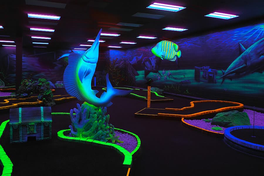 A black-light mini golf course with glowing sea creatures